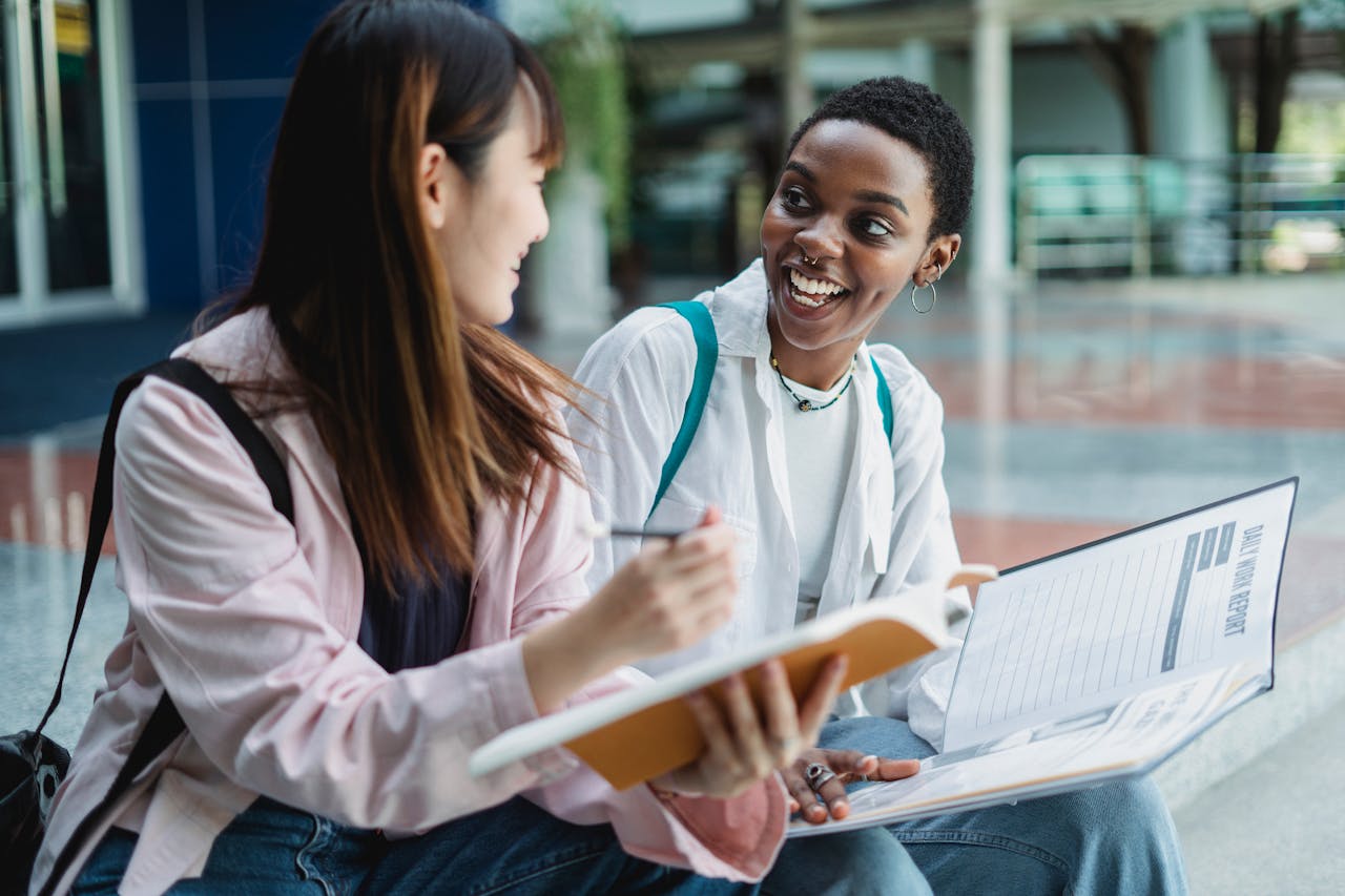 Two female students discussing and studying together outdoors, emphasizing collaboration and diversity.