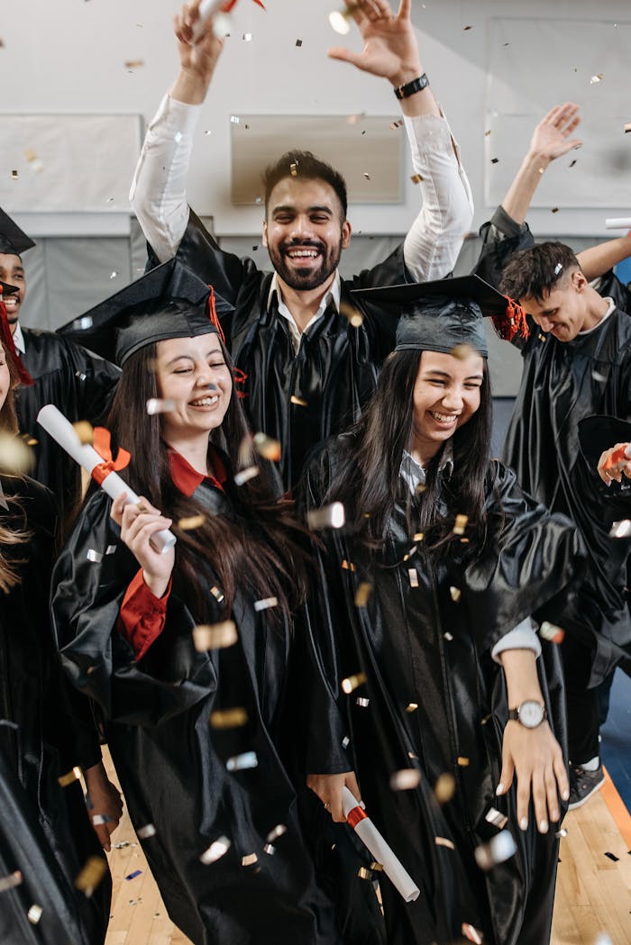 Group of diverse graduates celebrating their success with confetti indoors.